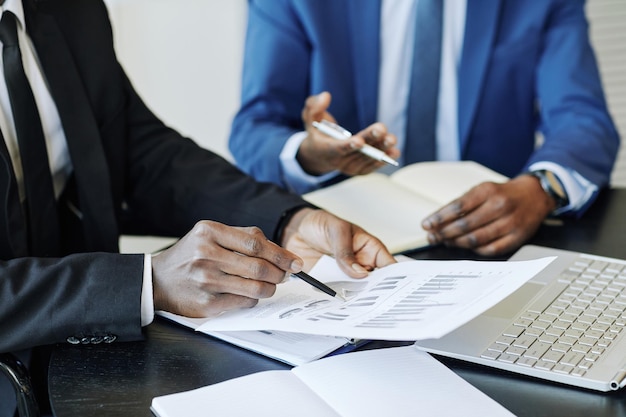 Close up of unrecognizable businessman analyzing data report in meeting and pointing at financial ch