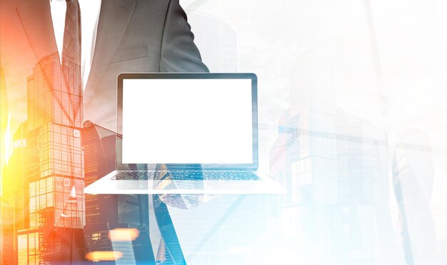 Close up of an unrecognizable businessman holding a laptop with a blank screen in a foggy city. Toned image, mock up