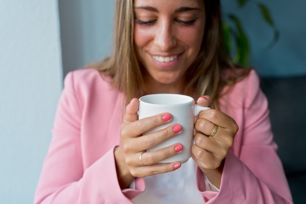 自宅で温かい飲み物を飲んでいる認識できない白人女性のクローズアップ。屋内で一杯のコーヒーを保持している女性の手の水平方向の詳細。屋内での女性のライフスタイル