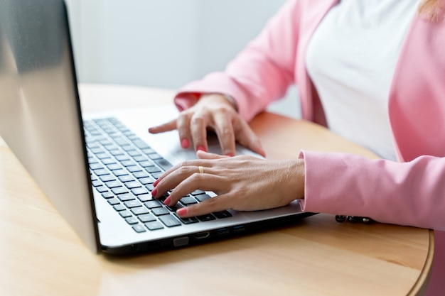 집에서 키보드로 일하는 알아볼 수 없는 백인 여성의 클로즈업. 실내 컴퓨터에 입력하는 여자 손의 수평 세부 사항. 온라인 작업 및 기술 개념입니다.