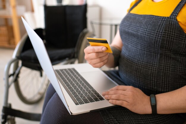 Foto primo piano di donna disabile irriconoscibile utilizzando laptop mentre si paga con carta di credito online