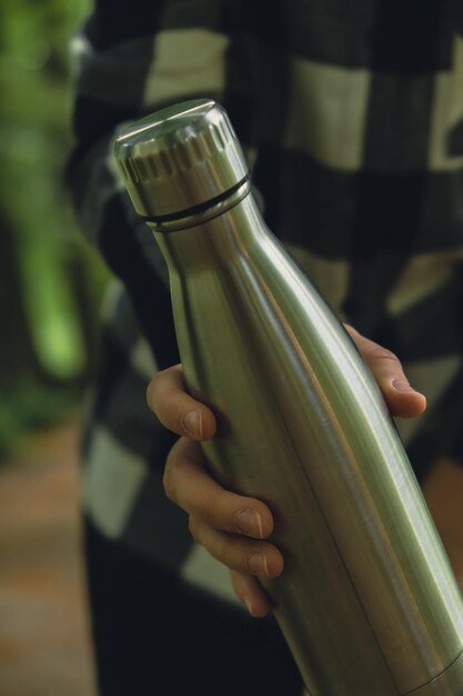 Photo close-up of unrecognizable female hand holding water bottle reusable steel thermo water bottle in