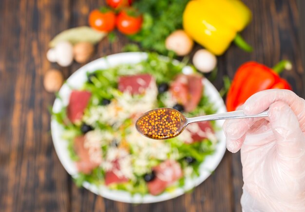 Close up of unrecognizable hand in glove holding spoon with dijon mustard