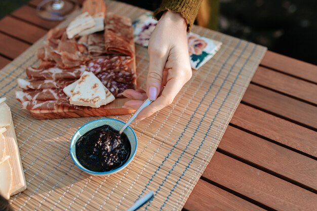 Close-up unrecognizable hand serving jam. Table set with appetizers and tasty food. Picnic concept.