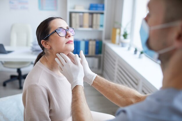 Close up of unrecognizable male doctor palpating throat of woman while examining female patient during consultation in clinic