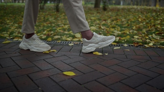 Close up unrecognizable man in white sneakers relaxing in city park Side shot of male legs walking on wet path in autumn nature Person spending free time in autumn background