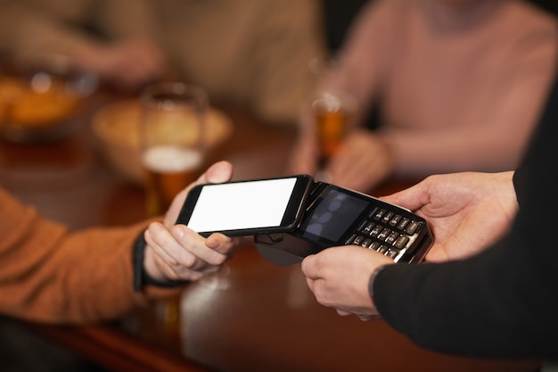 Close up of unrecognizable mature man paying via NFC with smartphone, focus on hand holding phone over terminal, copy space