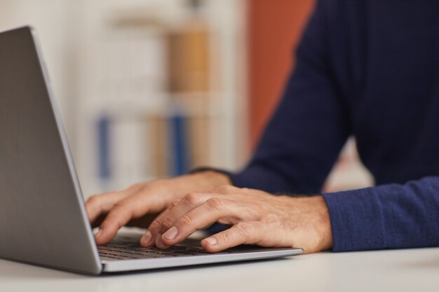 Закройте до неузнаваемости зрелого мужчины, использующего ноутбук во время работы в домашнем офисе, сосредоточьтесь на мужских руках, печатающих на клавиатуре, скопируйте пространство