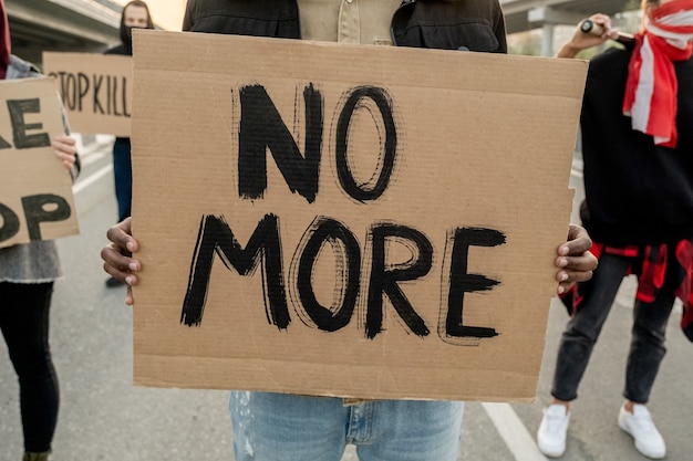 Close-up of unrecognizable person holding benner with No More words while participating in riot