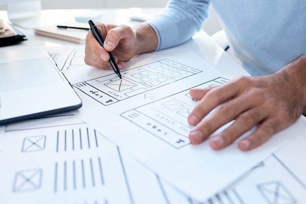 Close-up of unrecognizable UI engineer sitting at desk and making interface design for device