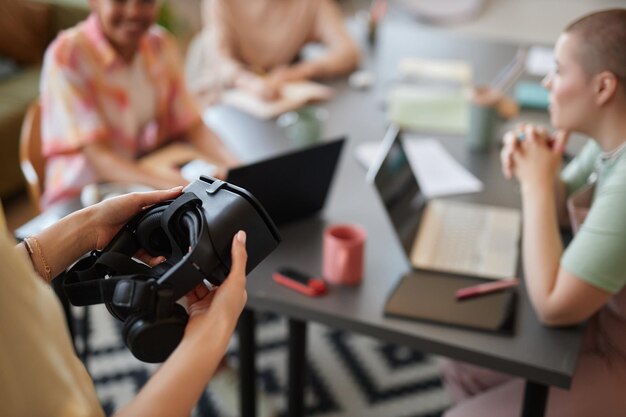 Photo close up of unrecognizable woman holding vr headset with blurred team meeting setting copy space