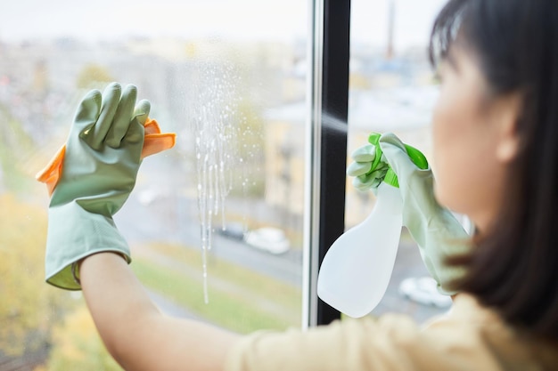 Close up of unrecognizable young woman cleaning windows with spray at home copy space