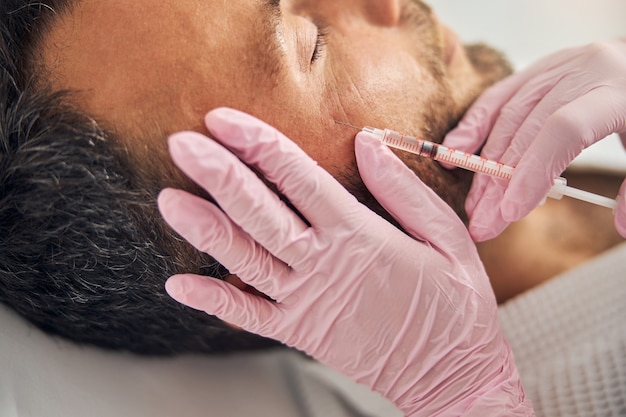 Primo piano di un giovane con la barba lunga che riceve un trattamento iniettabile per la cura della pelle al centro benessere wellness