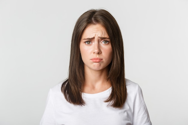 Close-up of upset and gloomy cute brunette girl sulking, looking miserable.