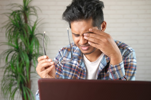 Close up of upset man suffering from strong eye pain while working on laptop