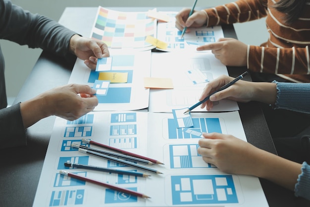 Close up ux developer and ui designer brainstorming about mobile app interface wireframe design on table with customer breif and color code at modern officeCreative digital development agency