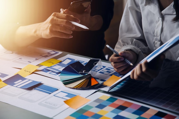 Close up ux developer and ui designer brainstorming about mobile app interface wireframe design on table with customer breif and color code at modern officeCreative digital development agency