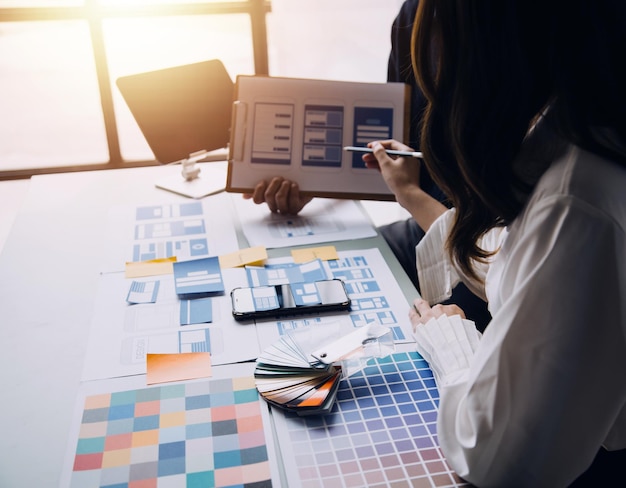 Close up ux developer and ui designer brainstorming about mobile app interface wireframe design on table with customer breif and color code at modern officeCreative digital development agency