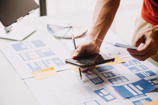 Close up ux developer and ui designer brainstorming about mobile app interface wireframe design on table with customer breif and color code at modern officeCreative digital development agency