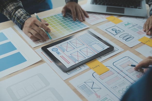 Photo close up ux developer and ui designer brainstorming about mobile app interface wireframe design on table with customer breif and color code at modern officecreative digital development agency