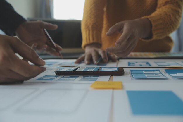 Close up ux developer and ui designer brainstorming about mobile app interface wireframe design on table with customer breif and color code at modern officeCreative digital development agency