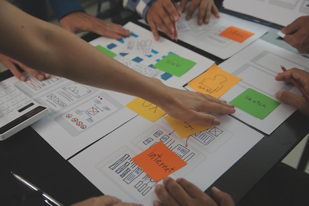 Close up ux developer and ui designer brainstorming about mobile app interface wireframe design on table with customer breif and color code at modern officeCreative digital development agency