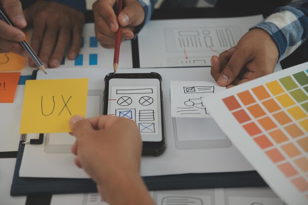 Крупным планом UX-разработчик и UI-дизайнер проводят мозговой штурм по поводу дизайна каркаса интерфейса мобильного приложения на столе с кратким описанием клиента и цветовым кодом в современном офисеАгентство креативного цифрового развития