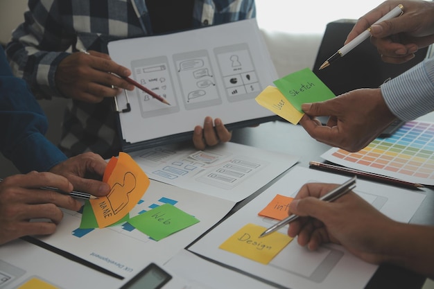 Close up ux developer and ui designer brainstorming about mobile app interface wireframe design on table with customer breif and color code at modern officeCreative digital development agency