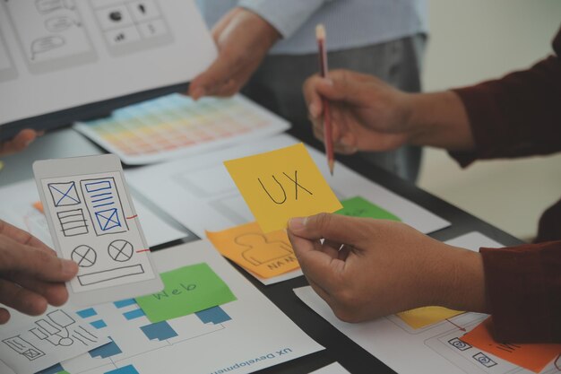 Close-up ux-ontwikkelaar en ui-ontwerper brainstormen over het draadframe-ontwerp van de mobiele app-interface op tafel met klantbreif en kleurcode bij modern kantoorCreatief digitaal ontwikkelingsbureau