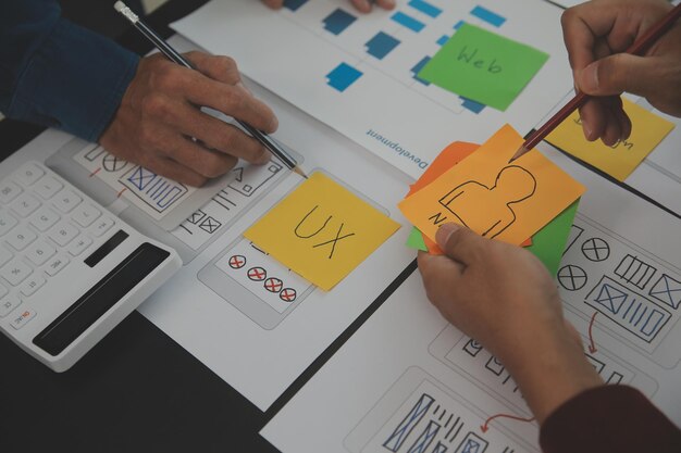 Close-up ux-ontwikkelaar en ui-ontwerper brainstormen over het draadframe-ontwerp van de mobiele app-interface op tafel met klantbreif en kleurcode bij modern kantoorCreatief digitaal ontwikkelingsbureau