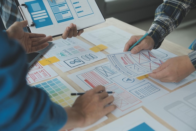 Close up ux-ontwikkelaar en ui-ontwerper brainstorming over mobiele app-interface wireframe-ontwerp op tafel met klantbreif en kleurcode bij modern kantoorCreatief digitaal ontwikkelingsbureau