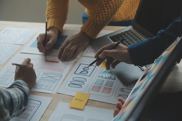 Close up ux-ontwikkelaar en ui-ontwerper brainstorming over mobiele app-interface wireframe-ontwerp op tafel met klantbreif en kleurcode bij modern kantoorCreatief digitaal ontwikkelingsbureau