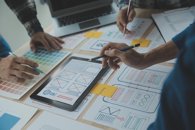 Close up ux-ontwikkelaar en ui-ontwerper brainstorming over mobiele app-interface wireframe-ontwerp op tafel met klantbreif en kleurcode bij modern kantoorCreatief digitaal ontwikkelingsbureau