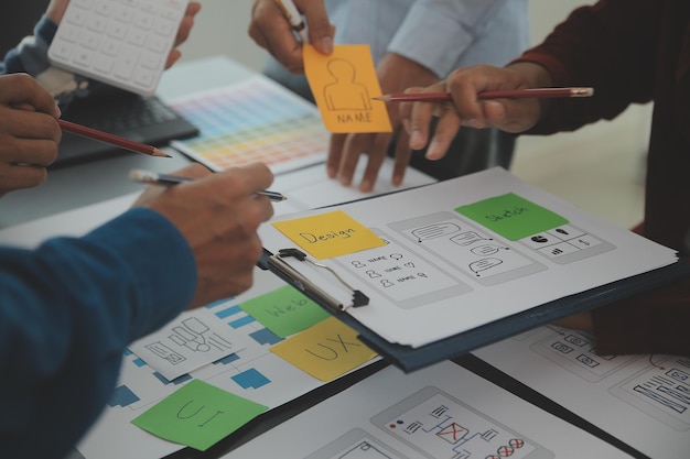 Close up ux-ontwikkelaar en ui-ontwerper brainstorming over mobiele app-interface wireframe-ontwerp op tafel met klantbreif en kleurcode bij modern kantoorCreatief digitaal ontwikkelingsbureau