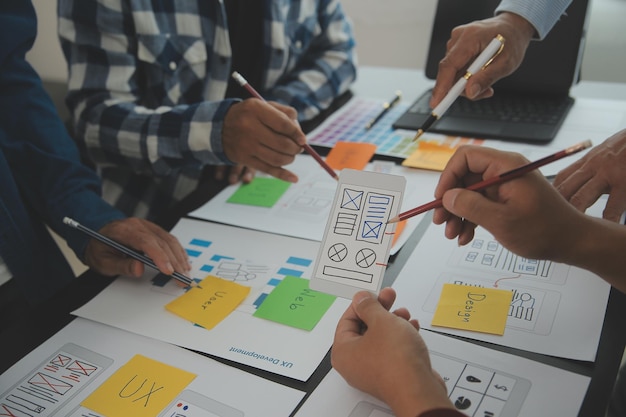 Close up ux-ontwikkelaar en ui-ontwerper brainstorming over mobiele app-interface wireframe-ontwerp op tafel met klantbreif en kleurcode bij modern kantoorCreatief digitaal ontwikkelingsbureau