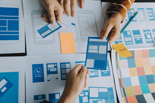 Close up ux-ontwikkelaar en ui-ontwerper brainstorming over mobiele app-interface wireframe-ontwerp op tafel met klantbreif en kleurcode bij modern kantoorCreatief digitaal ontwikkelingsbureau
