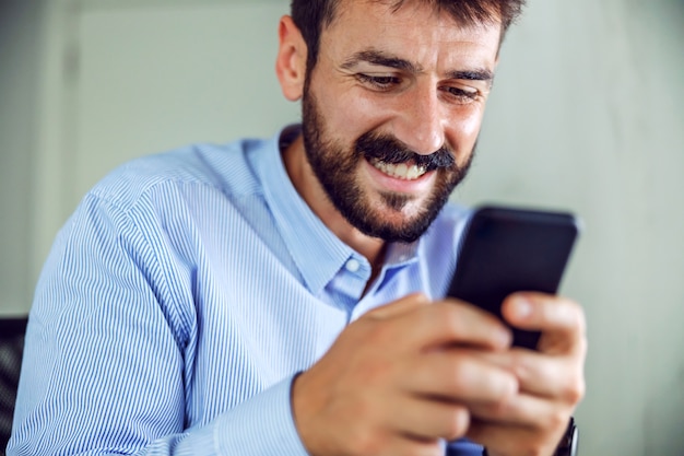 Close-up van aantrekkelijke glimlachende bebaarde zakenman die slimme telefoon houdt.