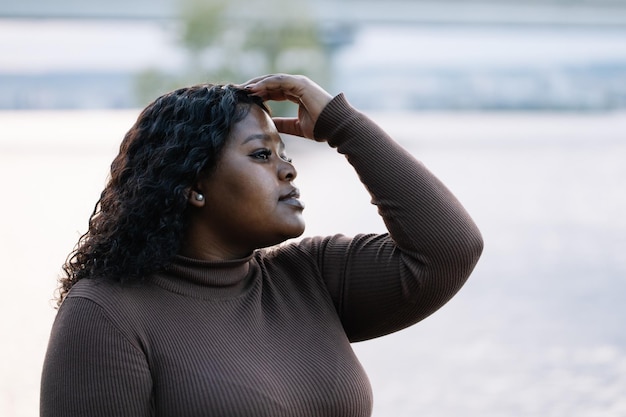 Close-up van aantrekkelijke poserende mollige, volslanke multiraciale vrouw in de buurt van zee of rivier op zomervakantie die haar aanraakt