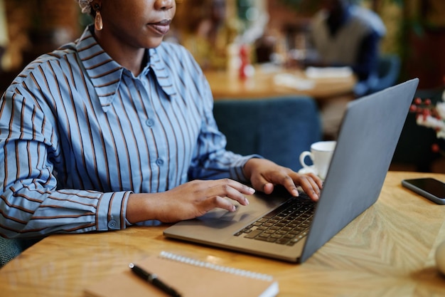 Close-up van Afrikaanse zakenvrouw die aan tafel zit en op laptop typt, ze werkt online in café