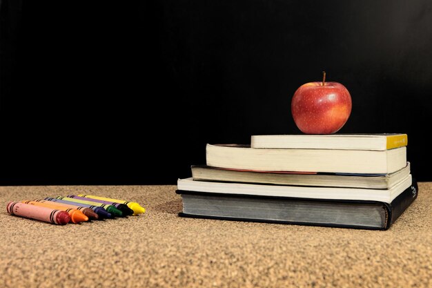 Close-up van appel op boeken met kleurpotloden tegen een zwarte achtergrond