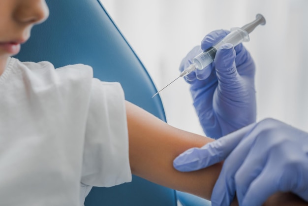 Foto close-up van arts die vaccin in de arm van de jongen injecteert in de kliniek