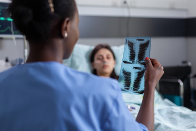 Close up van assistent met zwarte huid die longen radiografie uitlegt aan zieke vrouw