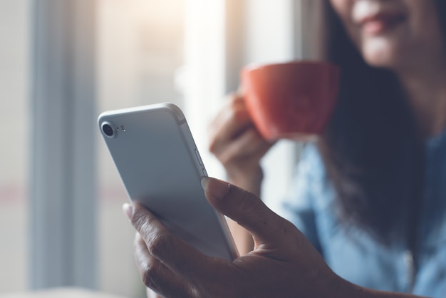 Close up van Aziatische vrouw met behulp van mobiele telefoon en koffie drinken