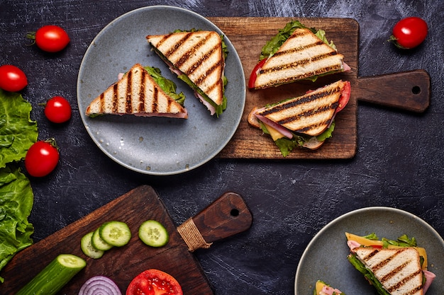 Close-up van bacon sandwitch met verse tomaten, de bladeren van de slasalade, komkommer en kaas, op donkerblauwe concrete rustieke lijstachtergrond, niemand. Bovenaanzicht.