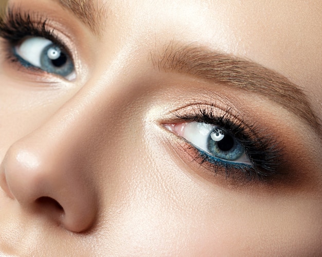 Close-up van blauwe vrouw oog met mooie gouden tinten en zwarte eyeliner make-up. Klassieke make-up. Perfecte wenkbrauwen.