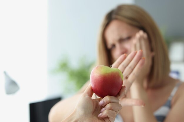 Close-up van blonde vrouw weigert appel te eten vanwege tandpijn. arme vrouwelijke dichte wang met hand, tandarts nodig. tandprobleem, gezondheidszorgconcept