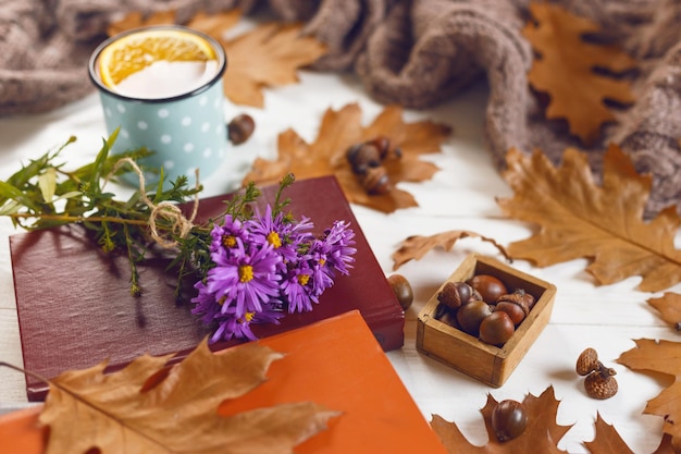 Close-up van boeken en kopje thee met oranje herfstbladeren warme sjaal op houten achtergrond