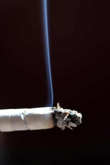Close-up van brandende sigaret met rook tegen zwarte achtergrond