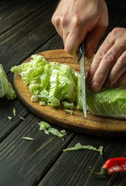 Close-up van chef-kok handen gesneden groene bladeren sla op een snijplank met mes