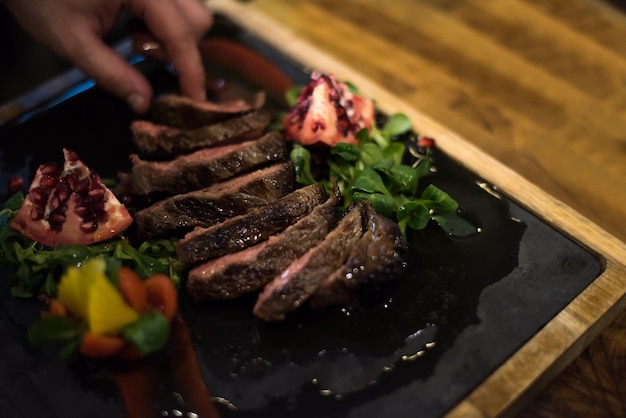 close-up van chef-kok handen in hotel of restaurant keuken serveren biefstuk met plantaardige decoratie
